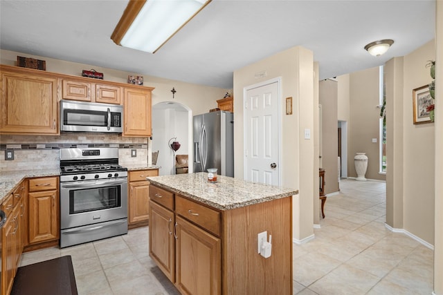 kitchen with decorative backsplash, a center island, light stone countertops, and stainless steel appliances