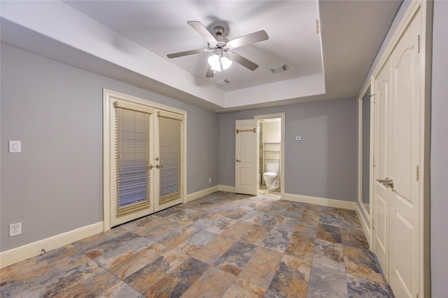 unfurnished bedroom featuring ceiling fan, a raised ceiling, and connected bathroom