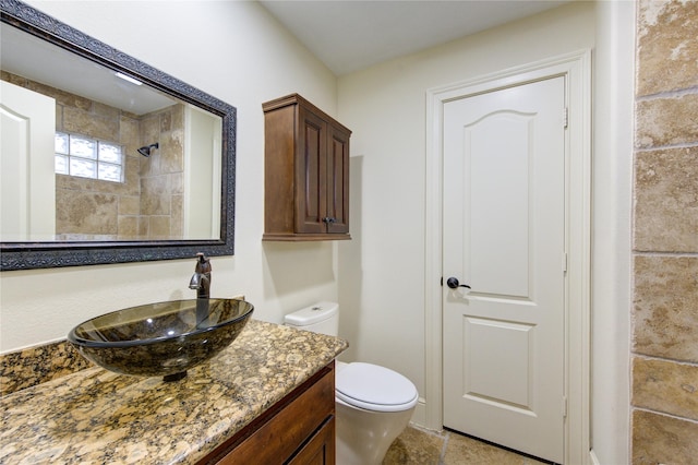 bathroom featuring a tile shower, vanity, and toilet