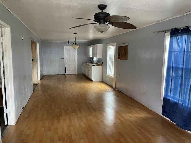 unfurnished living room with ceiling fan, sink, light hardwood / wood-style floors, and a textured ceiling