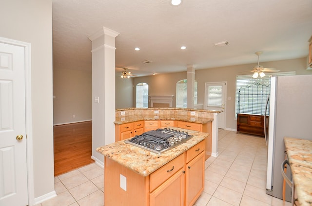 kitchen with white fridge, a kitchen island, light tile patterned floors, and stainless steel gas cooktop