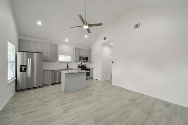 kitchen featuring decorative backsplash, gray cabinetry, stainless steel appliances, ceiling fan, and a kitchen island