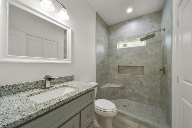 bathroom with a tile shower, vanity, and toilet