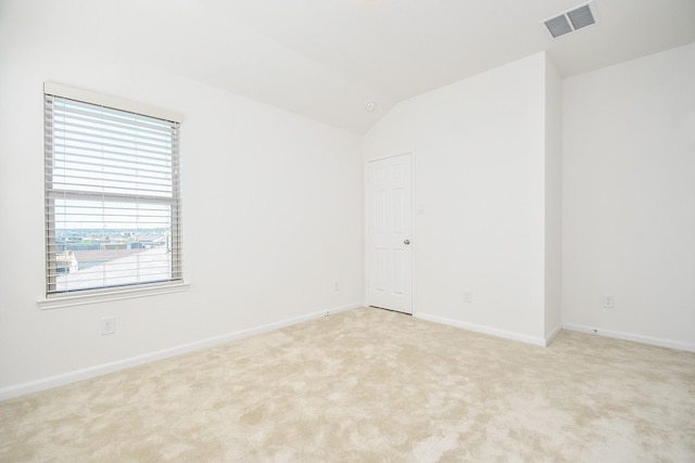 spare room featuring light carpet, vaulted ceiling, visible vents, and baseboards