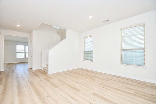 spare room with stairs, light wood-style flooring, visible vents, and baseboards