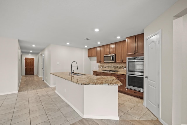 kitchen with light stone counters, sink, stainless steel appliances, and an island with sink