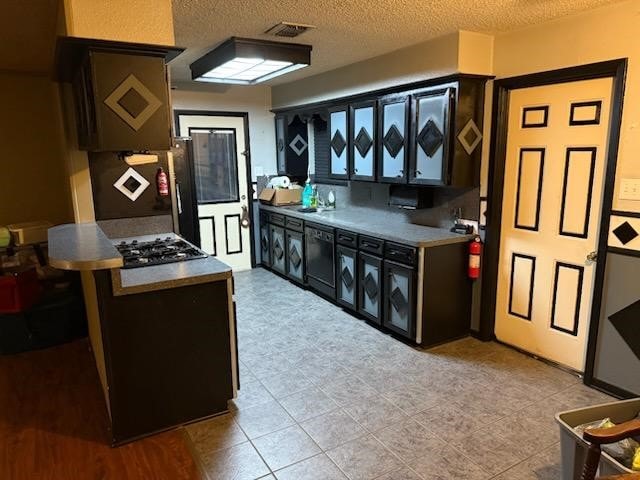 kitchen featuring a textured ceiling, stainless steel gas cooktop, sink, black dishwasher, and washer / clothes dryer