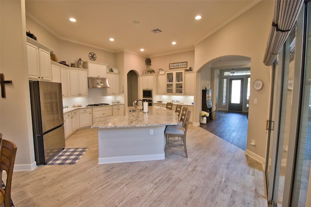 kitchen featuring stainless steel appliances, white cabinetry, light wood-type flooring, ornamental molding, and an island with sink