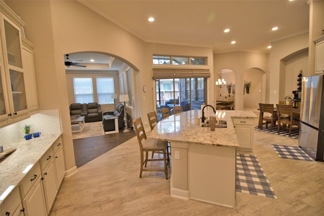 kitchen featuring a center island with sink, stainless steel refrigerator, light wood-type flooring, light stone counters, and sink