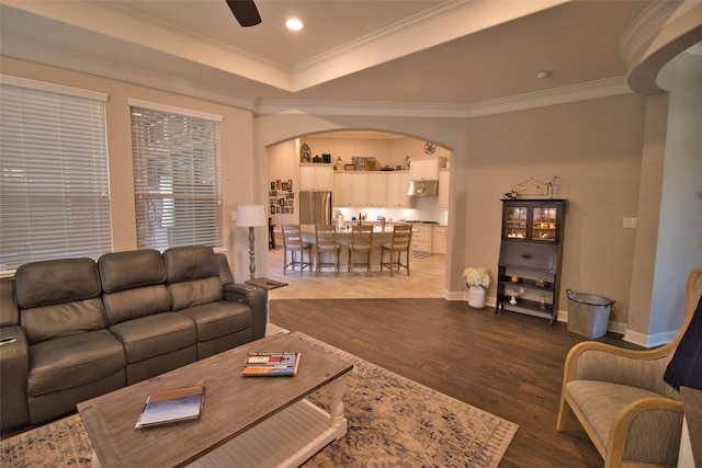 living room featuring ceiling fan, dark wood-type flooring, ornamental molding, and a raised ceiling