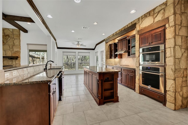 kitchen with dark stone counters, a center island with sink, sink, decorative backsplash, and stainless steel appliances