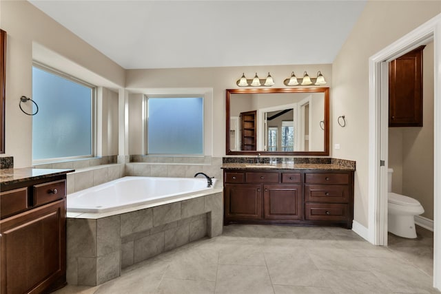 bathroom featuring vanity, a relaxing tiled tub, toilet, and plenty of natural light