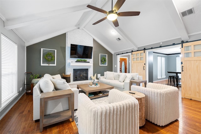 living room featuring ceiling fan, hardwood / wood-style flooring, a barn door, and vaulted ceiling with beams