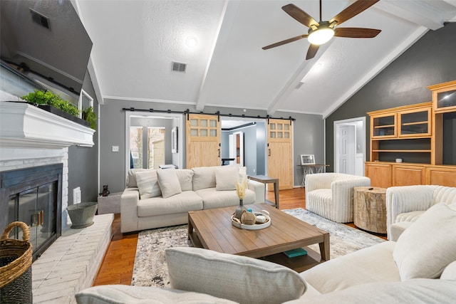 living room with light wood-type flooring, lofted ceiling with beams, a brick fireplace, and a barn door