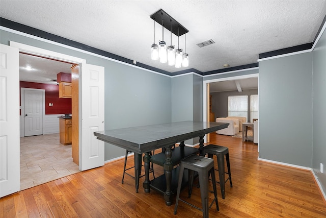 dining area with light hardwood / wood-style floors, a textured ceiling, and ornamental molding