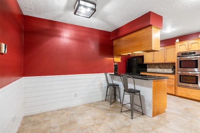 kitchen with kitchen peninsula, appliances with stainless steel finishes, a kitchen bar, a textured ceiling, and decorative backsplash