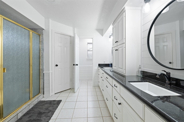 bathroom with a textured ceiling, tile patterned flooring, a shower with shower door, and vanity