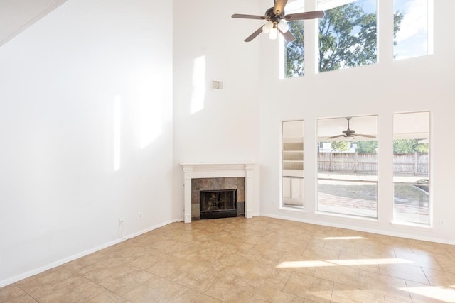 unfurnished living room with light tile patterned floors, a towering ceiling, ceiling fan, and a tiled fireplace