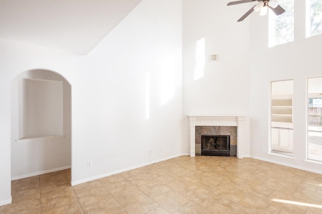 unfurnished living room featuring a tile fireplace, a wealth of natural light, ceiling fan, and a high ceiling