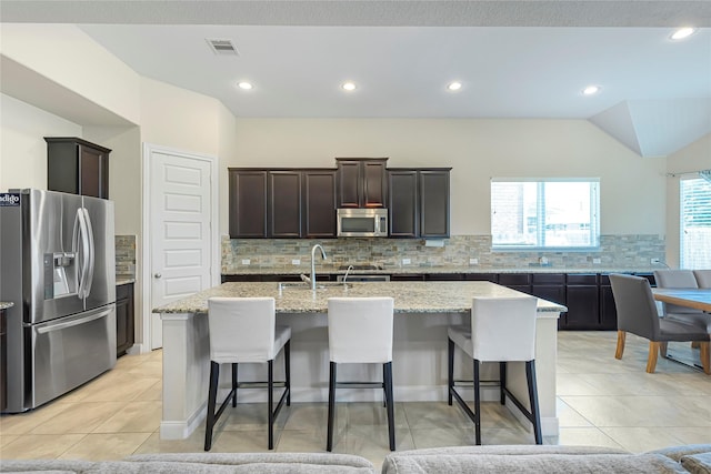 kitchen featuring sink, tasteful backsplash, a center island with sink, light tile patterned floors, and appliances with stainless steel finishes