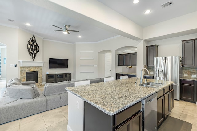 kitchen with a center island with sink, sink, ceiling fan, a fireplace, and stainless steel appliances