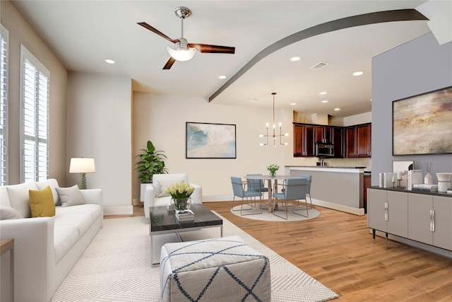 living room featuring ceiling fan with notable chandelier and light hardwood / wood-style flooring