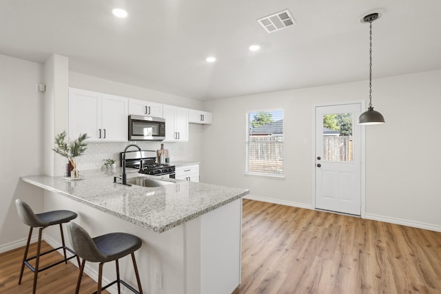 kitchen with kitchen peninsula, decorative light fixtures, light stone counters, white cabinetry, and stainless steel appliances