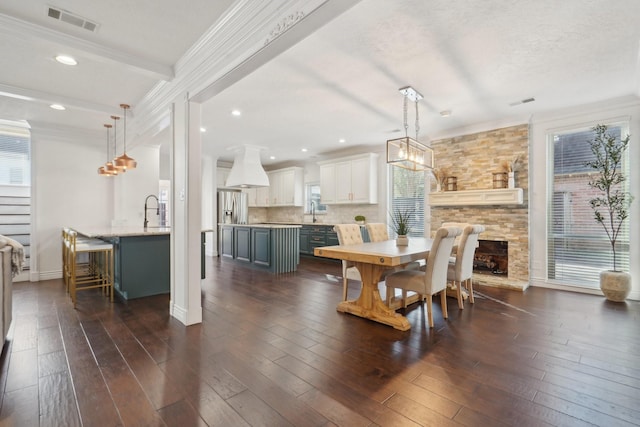 dining area featuring beam ceiling, sink, dark hardwood / wood-style floors, a fireplace, and ornamental molding