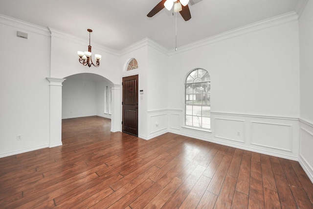 empty room with ceiling fan with notable chandelier, dark hardwood / wood-style flooring, decorative columns, and ornamental molding