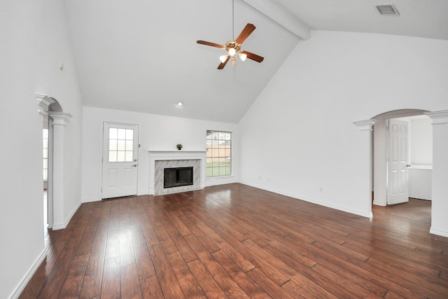 unfurnished living room with a high end fireplace, decorative columns, ceiling fan, dark wood-type flooring, and beam ceiling