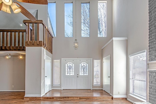 entryway featuring hardwood / wood-style flooring, ceiling fan, beam ceiling, and a towering ceiling