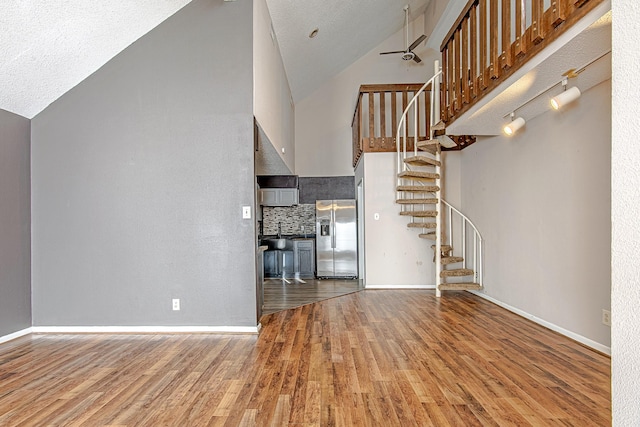 unfurnished living room featuring a textured ceiling, hardwood / wood-style flooring, high vaulted ceiling, and ceiling fan