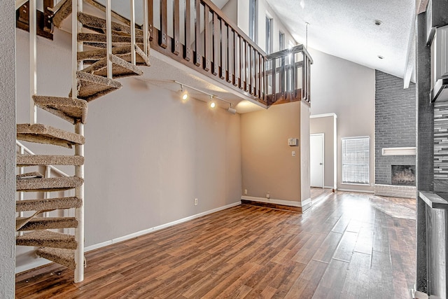 unfurnished living room with hardwood / wood-style flooring, a textured ceiling, high vaulted ceiling, and a brick fireplace