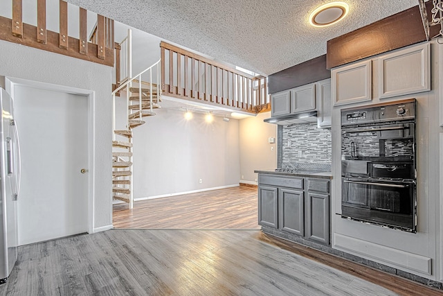 kitchen featuring tasteful backsplash, light hardwood / wood-style floors, a textured ceiling, gray cabinets, and black appliances