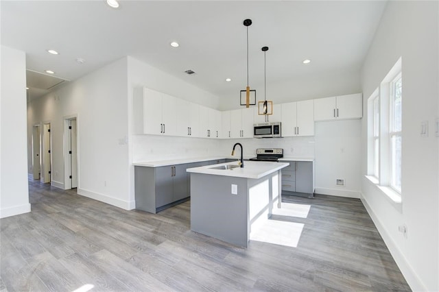 kitchen featuring sink, appliances with stainless steel finishes, tasteful backsplash, an island with sink, and decorative light fixtures