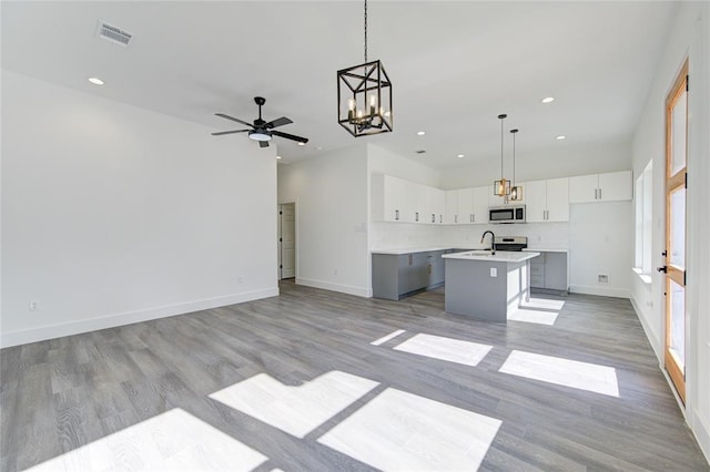 kitchen featuring a kitchen island with sink, hanging light fixtures, light hardwood / wood-style floors, white cabinets, and ceiling fan with notable chandelier