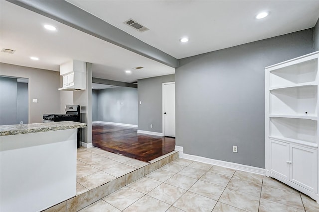 kitchen featuring light tile patterned flooring, black gas stove, white cabinetry, and built in features