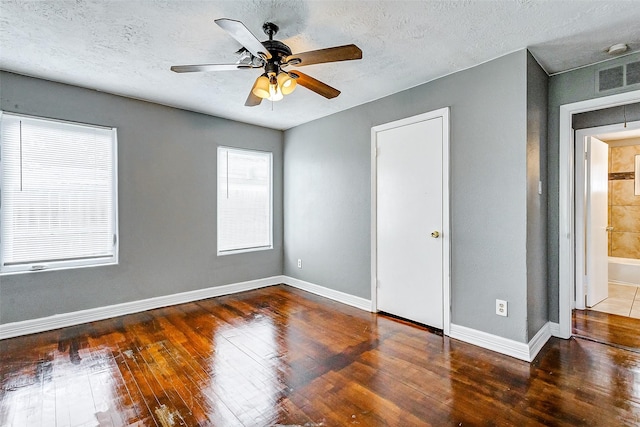 unfurnished bedroom featuring a textured ceiling, connected bathroom, dark hardwood / wood-style floors, and ceiling fan