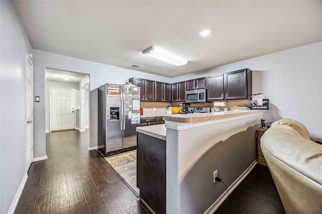 kitchen with kitchen peninsula, a breakfast bar, dark brown cabinets, stainless steel appliances, and hardwood / wood-style flooring