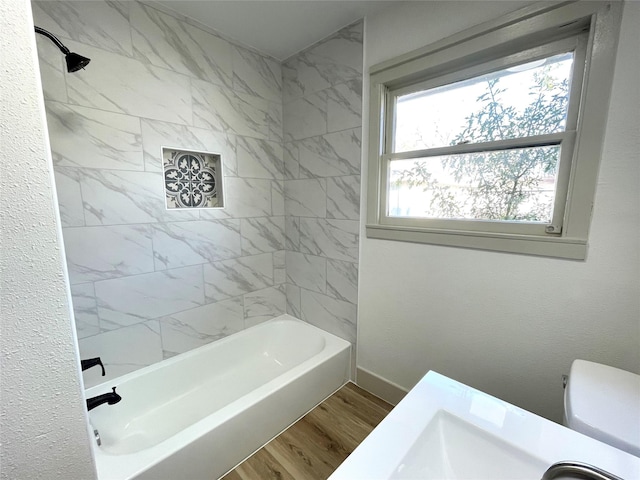 bathroom with tiled shower / bath combo, hardwood / wood-style flooring, and toilet