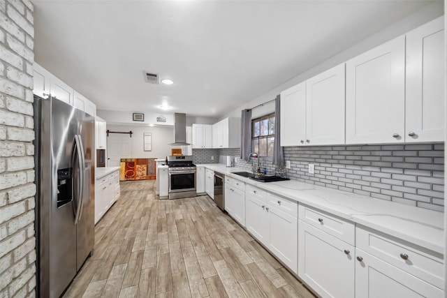 kitchen featuring wall chimney exhaust hood, a barn door, appliances with stainless steel finishes, tasteful backsplash, and white cabinetry