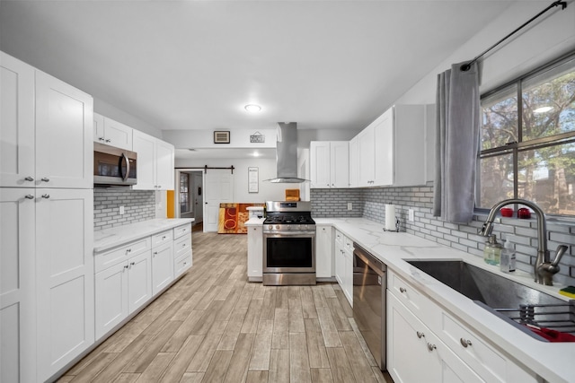 kitchen with white cabinetry, sink, stainless steel appliances, and wall chimney range hood