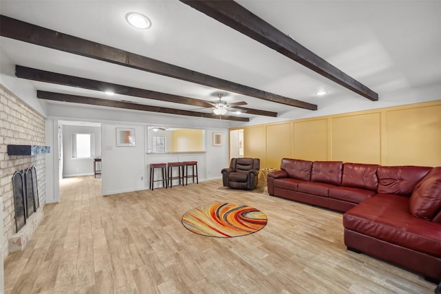 living room featuring a fireplace, wood-type flooring, ceiling fan, and beam ceiling