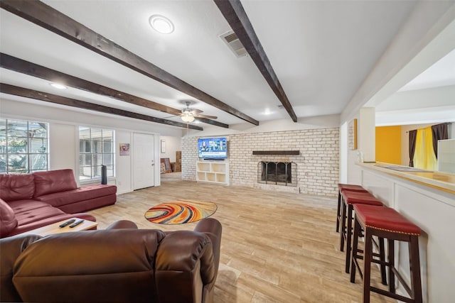 living room with beam ceiling, ceiling fan, light hardwood / wood-style flooring, and a brick fireplace