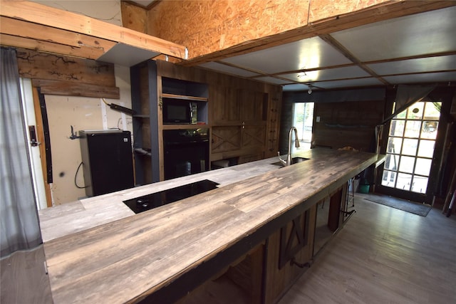 kitchen featuring black appliances, wood counters, light wood-type flooring, and sink