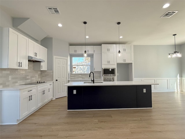 kitchen featuring stainless steel microwave, a center island with sink, pendant lighting, sink, and white cabinetry