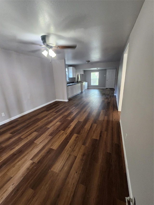 unfurnished living room featuring ceiling fan and dark wood-type flooring