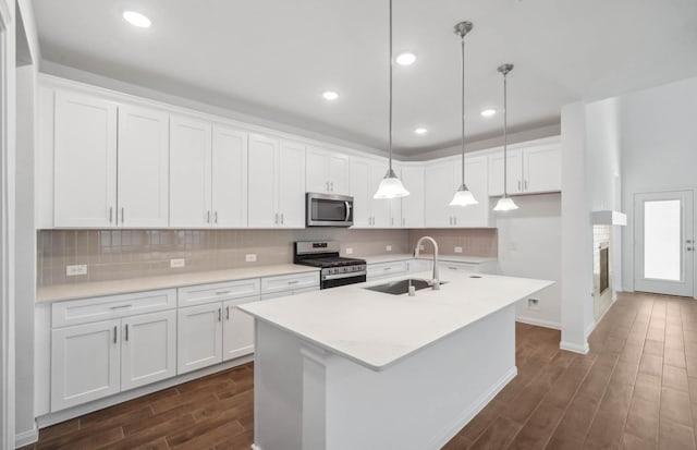 kitchen featuring stainless steel appliances, a kitchen island with sink, sink, white cabinetry, and hanging light fixtures