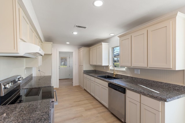 kitchen featuring appliances with stainless steel finishes, light hardwood / wood-style floors, dark stone counters, and sink