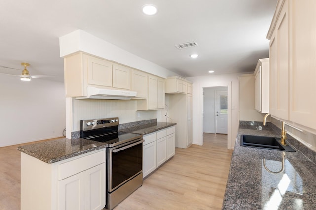 kitchen featuring light wood-type flooring, stainless steel range with electric stovetop, ceiling fan, sink, and dark stone countertops